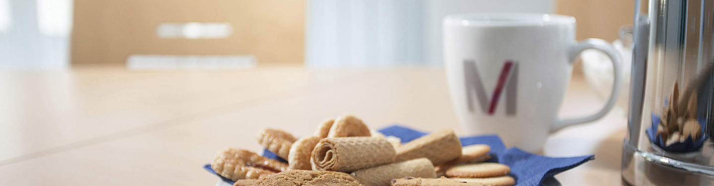 Conferences, meetings and workshops Close-up of a conference table setup at Munich Airport with a cup, a plate of cookies, and a coffee pot; creating a welcoming, calm atmosphere