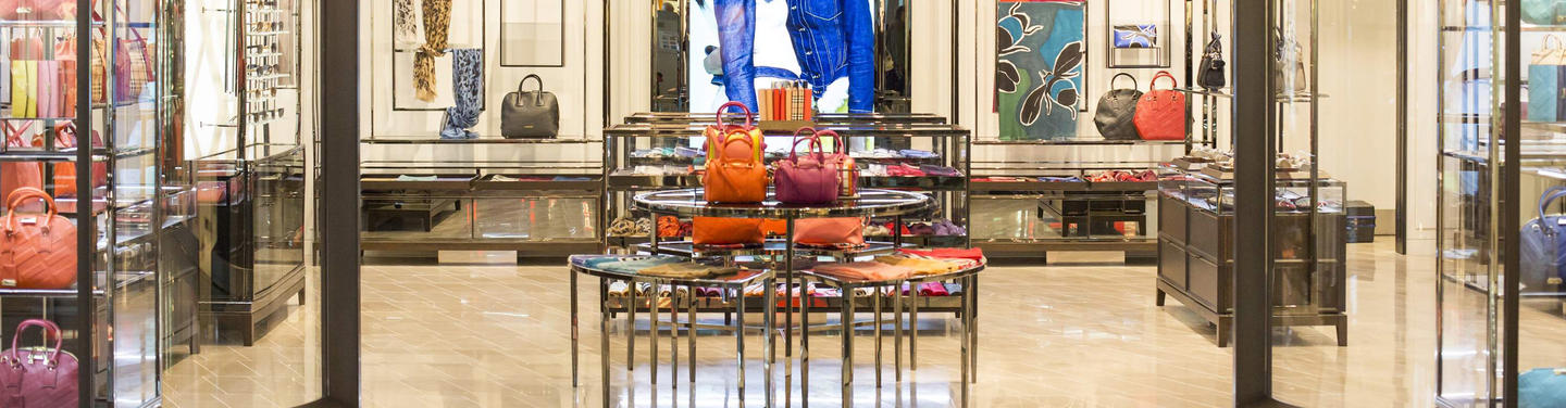 Burberry Einzelhandel Blick in ein elegant beleuchtetes Geschäft am Flughafen München mit farbigen Handtaschen, Accessoires und Auslagen auf gläsernen Tischen; ordentliche, hochwertige Einkaufsatmosphäre.