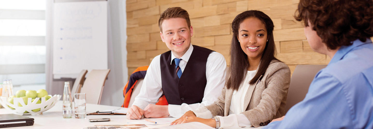 Strategy 2025 Three people are sitting at a table in a bright room, chatting cheerfully with each other—a typical job interview or consultation situation. The scene conveys professionalism, a welcoming culture, and a modern HR working environment.