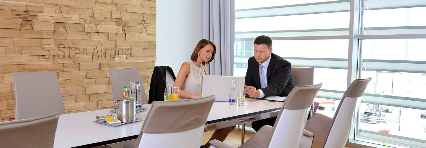 Five Star Airport Employees sit in a bright, modern conference room with large windows and discuss documents. The professional atmosphere stands for efficient work and business services at Munich Airport.