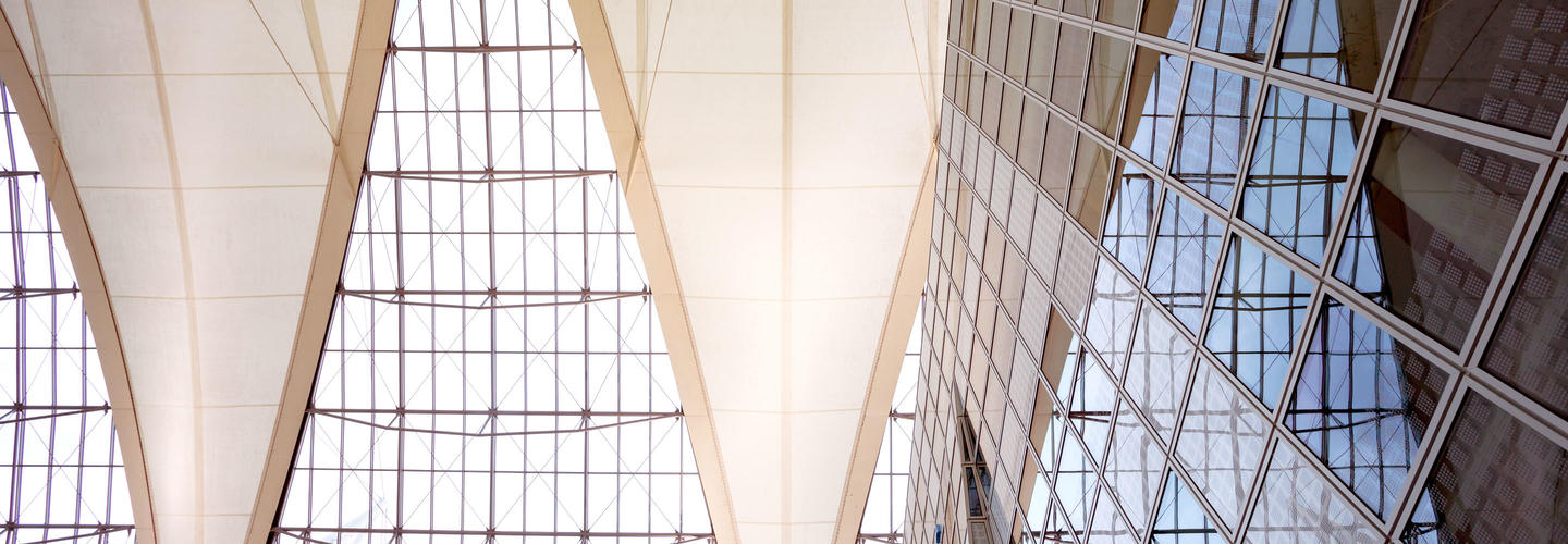 Immobilien & Vermietung Detailaufnahme der beeindruckenden Dach- und Glasarchitektur des Munich Airport Centers, mit hohen, hellen Decken und filigranen Trägerstrukturen. Das Bild betont Modernität, Transparenz und architektonische Eleganz.