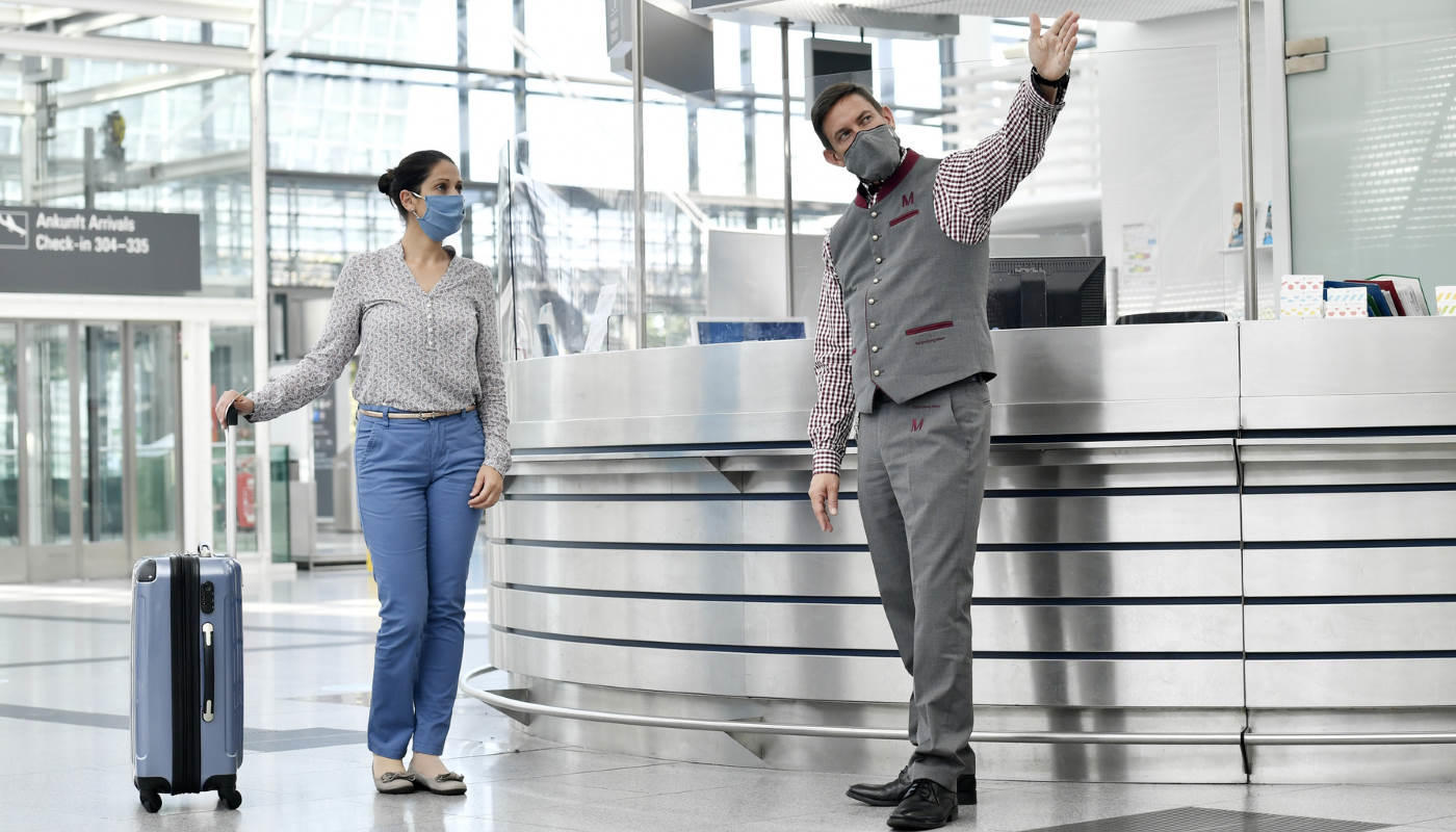 Passenger information desk Airport staff explaining directions to passenger - both wearing masks.