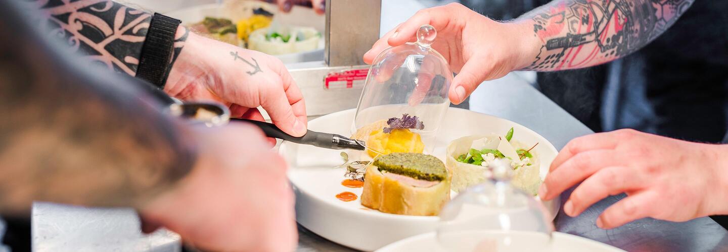 Kulinarische Highlights Nahaufnahme von Köchen, die mit viel Liebe zum Detail hochwertige Gerichte vorbereiten. Frische Zutaten und sorgfältige Handgriffe betonen die kulinarische Qualität und Professionalität der Gastronomie am Flughafen München.