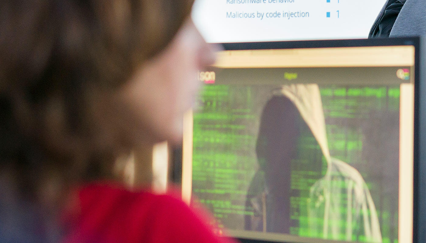 Hacking Workshop im ISH am Flughafen München Workshop-Teilnehmerin blickt auf einen Computerbildschirm, der die vermummte Gestalt eines Hackers zeigt.