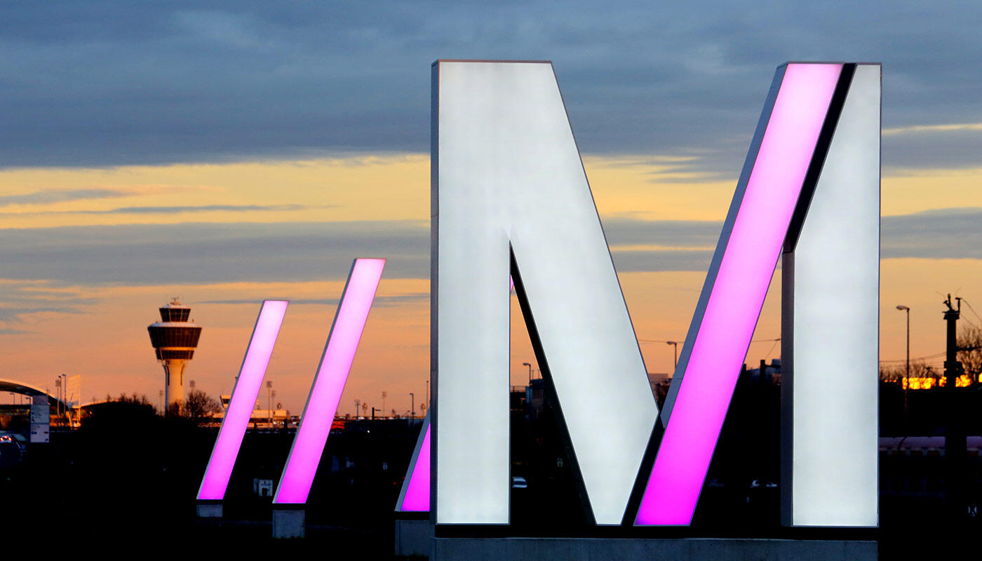 Directions to Munich Airport Luminated M-logo with the tower in the background on the approach road to Munich Airport
