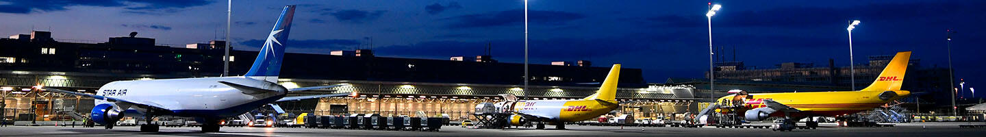 Nighttime Cargo Handling Several cargo aircraft parked on a brightly lit apron at night, with ground equipment and containers being moved.