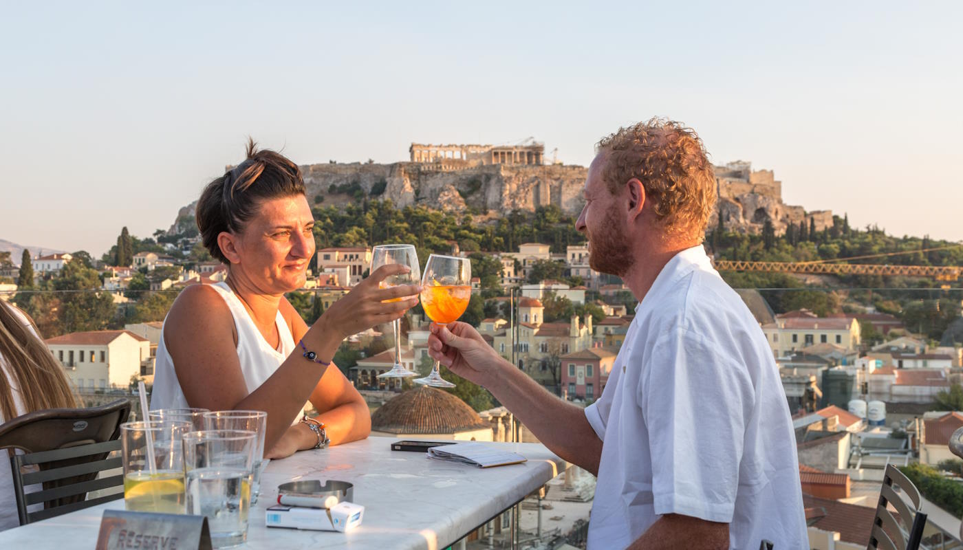 Paar vor der Akropolis in Athen – Romantischer Ausblick Paar stößt mit Getränken an vor der Akropolis in Athen
