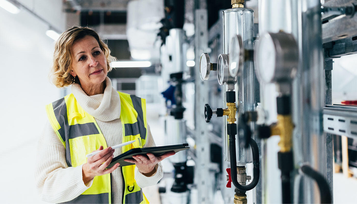 Ingenieurin der Gebäudetechnik am Flughafen München Person in gelber Warnweste hält ein Tablet und überprüft technische Anlagen.