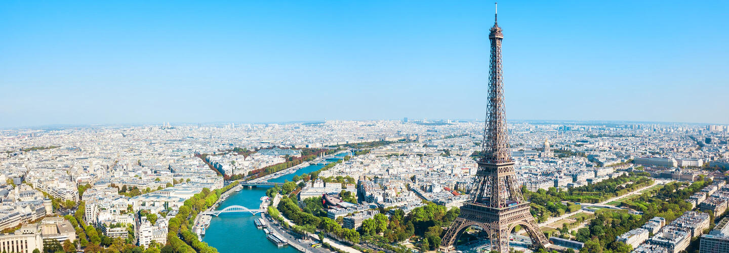 Verliebt in Paris Weite Panoramaaufnahme von Paris bei klarem Himmel, mit dem Eiffelturm im Zentrum und der Seine, die sich durch die Stadt schlängelt. Die Szene vermittelt Weite, Urbanität und den eleganten Charme der französischen Hauptstadt.