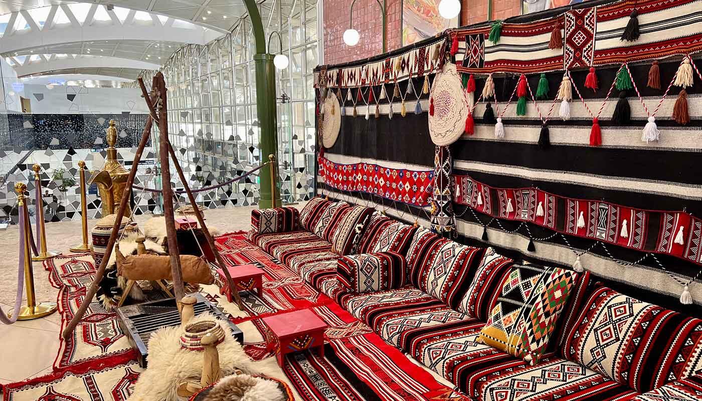 Arabische Sitzgruppe am Flughafen Riyadh Traditionelle arabische Sitzgruppe mit roten, schwarzen und weißen Mustern, dekorativen Textilien und Artefakten im Terminal 4 des King Khalid International Airport.