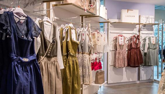 Verschiedene Dirndl lang und knielang in den Farben blau, grau, olivegrün, silber, altrosa und burgung hängen an Kleiderstangen. Außerdem sind einige Dirndlblusen zu sehen.
