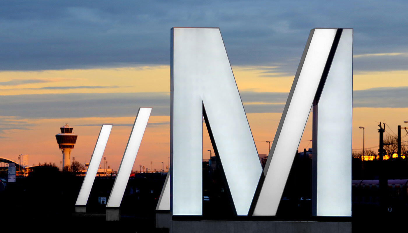Directions to Munich Airport Luminated M-logo with the tower in the background on the approach road to Munich Airport