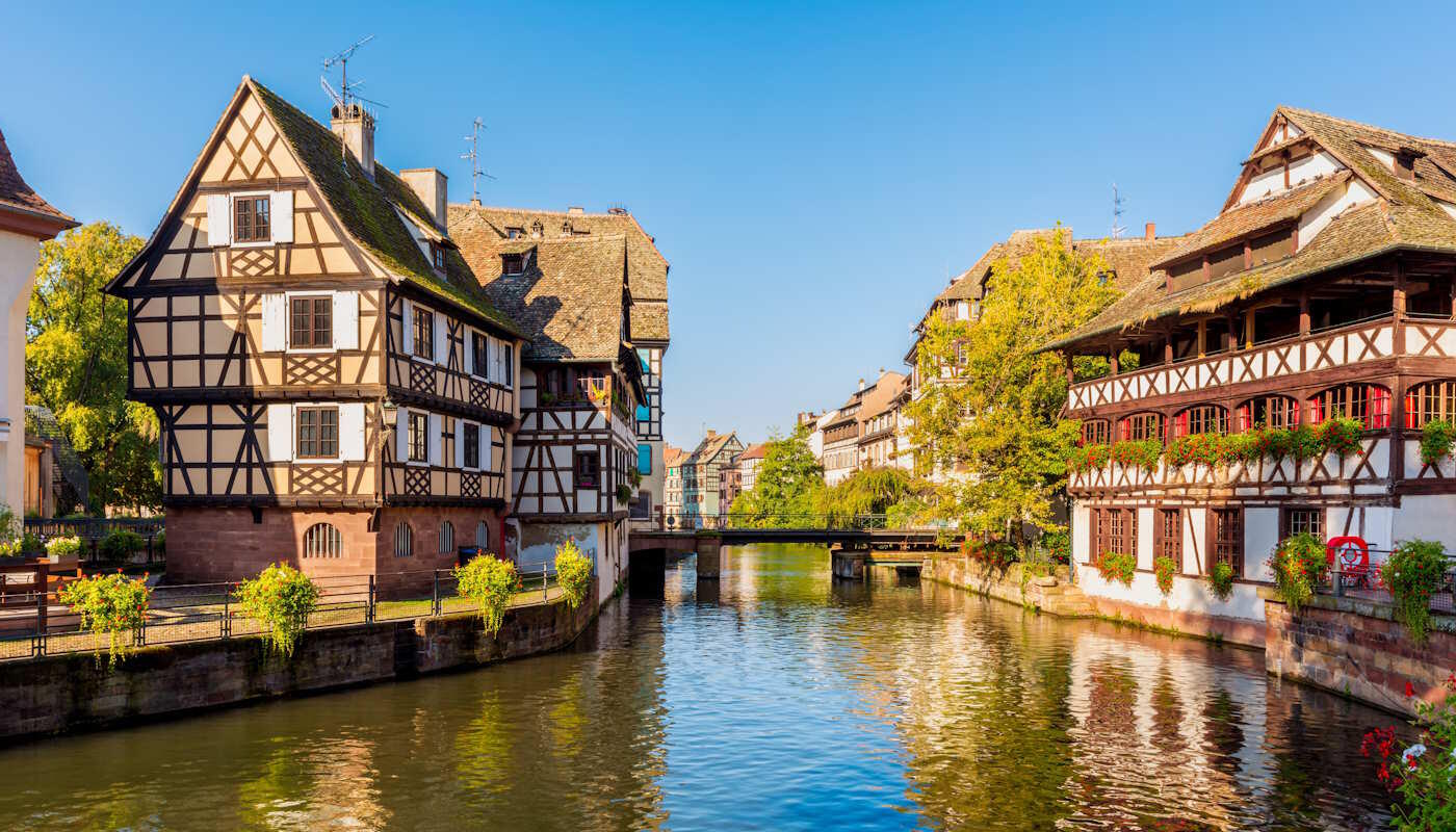 Fachwerkäuser in Straßburg, Frankreich Fachwerkhäuser am Fluss Ill in Straßburg, Frankreich. An den Ufern blühen Blumen und Sträucher, weiter hinten führt eine Brücke über den Fluss.