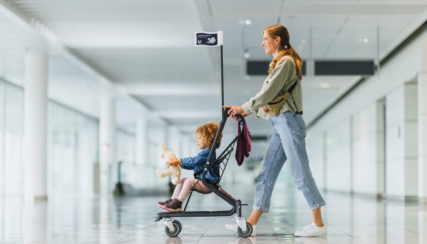 Entspannt reisen mit Kindern - kostenloser Buggy-Verleih am Flughafen Eine Mutter schiebt ihr Kind in einem Buggy durch einen modernen, hellen Flughafenbereich. Beide wirken entspannt, während sie durch das Terminal gehen.