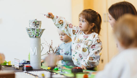 Kinder spielen an einem gebastelten Flughafenmodell, während ein Kind ein kleines Flugzeug über den Tower hält.