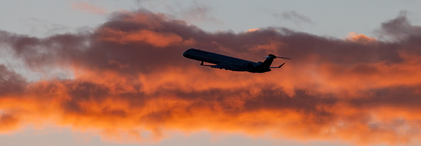 Flugzeug bei Sonnenuntergang Airplane ascends into the sky against orange-colored clouds at sunset.