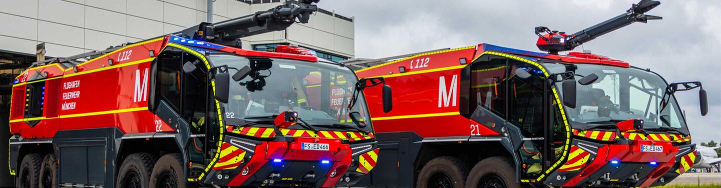 Ausbildung Werkfeuerwehr am Flughafen München Zwei große rote Flughafen‑Löschfahrzeuge stehen nebeneinander auf dem Vorfeld.