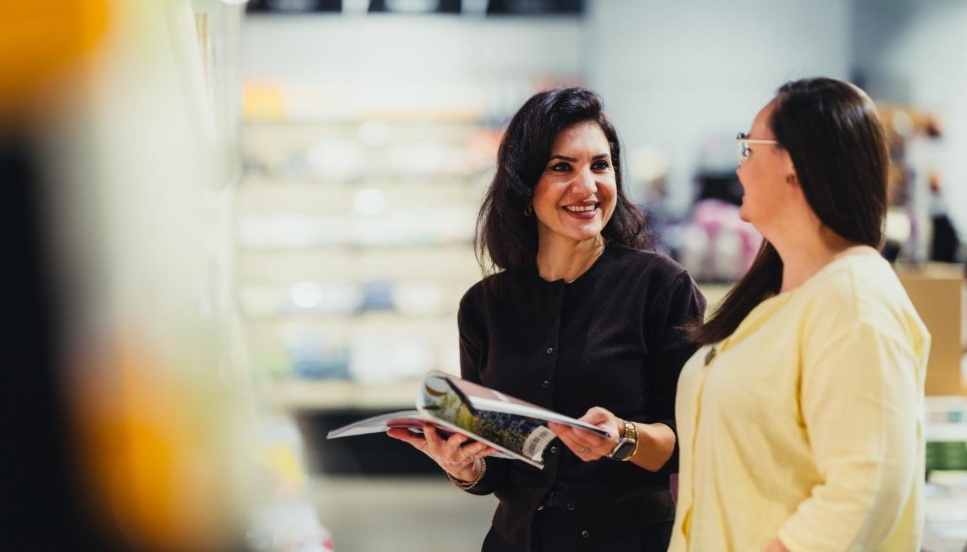 Floor Managerin berät Kundin kompetent im Einzelhandel Eine engagierte Floor Managerin lächelt freundlich, während sie eine Kundin individuell berät – die Szene wirkt vertrauensvoll, kompetent und angenehm entspannt.