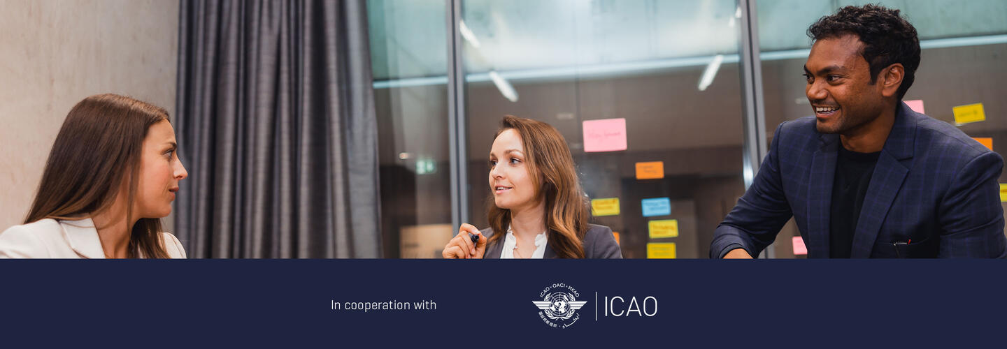 ICAO Training Developers Course at the Munich AirportAcademy Three people in a workshop setting in front of a glass wall with multiple colorful sticky notes; a dark banner at the bottom shows the text “In cooperation with” and the ICAO logo.
