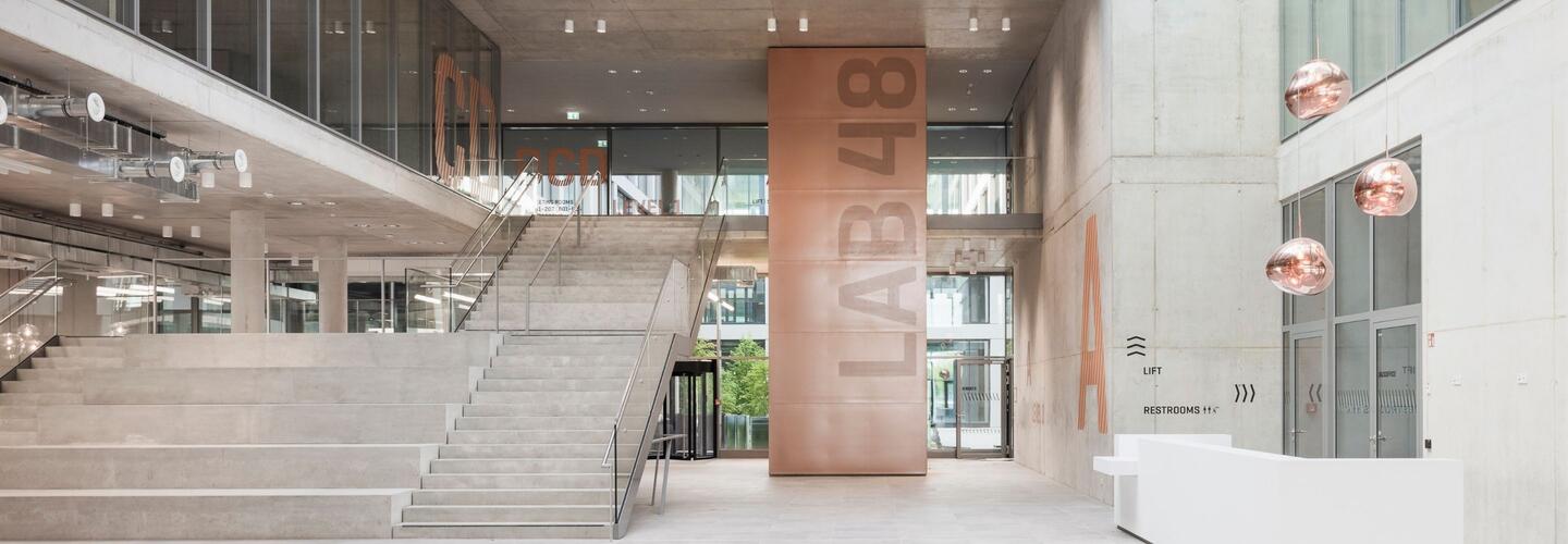 Modern Architecture and Inspiring Business Atmosphere at LabCampus Munich Bright and modern interior of LabCampus at Munich Airport featuring a spacious staircase, large glass fronts, elegant copper design elements, and an inspiring business atmosphere with contemporary architecture.