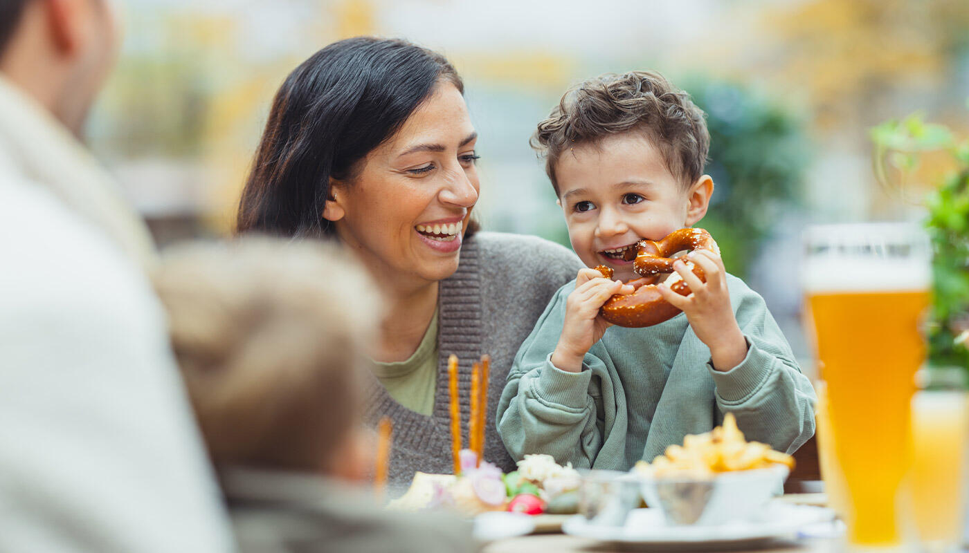 Family time at Airbräu Family time at Airbräu: A child eats a pretzel at a table in the beer garden at Munich Airport, while his mother sits smiling beside him.