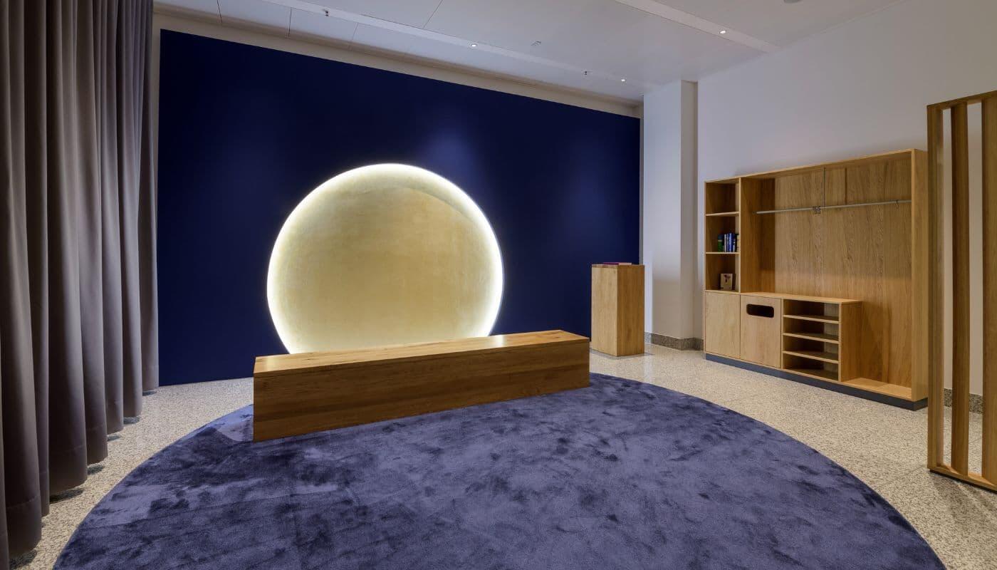 Prayer and Quiet Room at Terminal 1 Pier, Munich Airport Bright interfaith Prayer and Quiet Room at Munich Airport's Terminal 1 Pier featuring an illuminated circular artwork, warm wood furnishings, and a calm, welcoming atmosphere. The space provides travelers with a peaceful place for Muslim Salah, Christian and Jewish prayer, meditation, and quiet reflection before or after their journey.