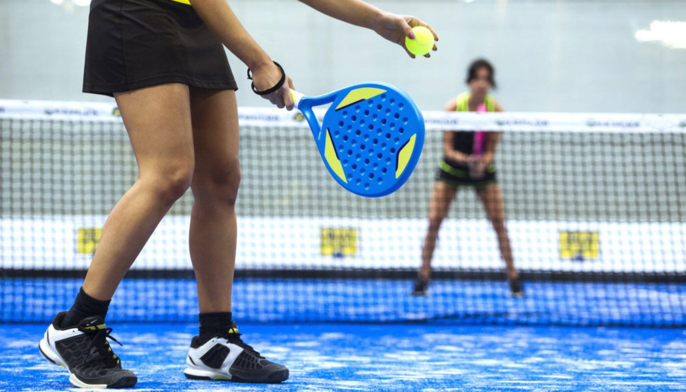 Padel-Spiel Padel-Szene auf einem modernen Court: Spielerin mit Padel-Schläger beim Ballwechsel auf blauem Spielfeld vor dem Netz.