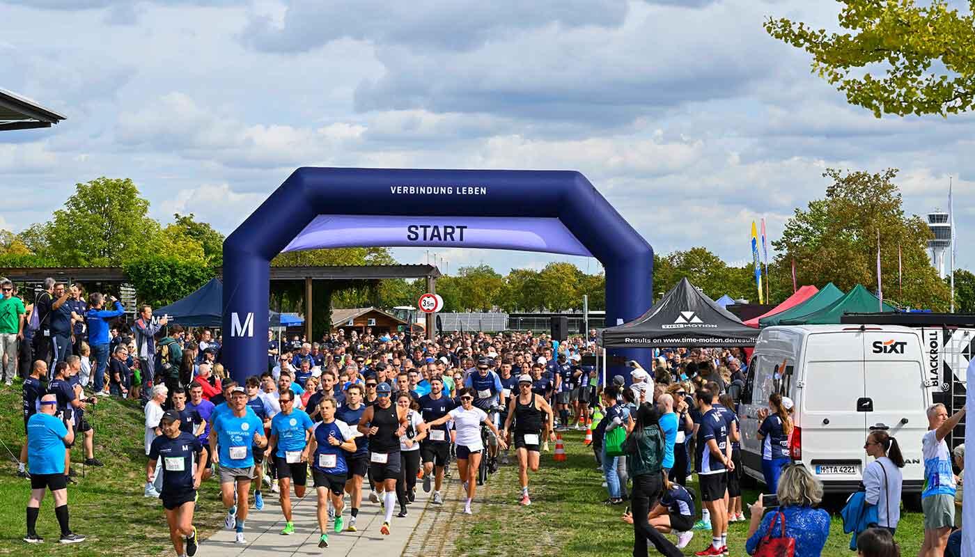 20. Airportlauf Großes Teilnehmerfeld beim Start des Airportlaufs auf dem Flughafengelände unter einem Startbogen mit der Aufschrift 'Verbindung leben'